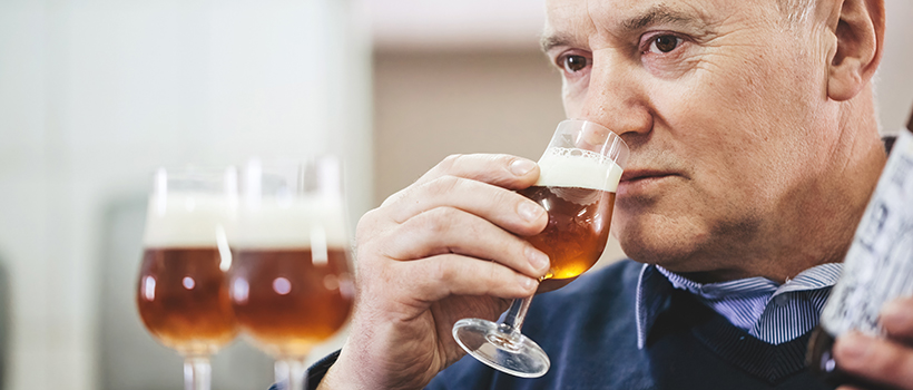 Man holding and smelling beer in glass with more beer in foreground