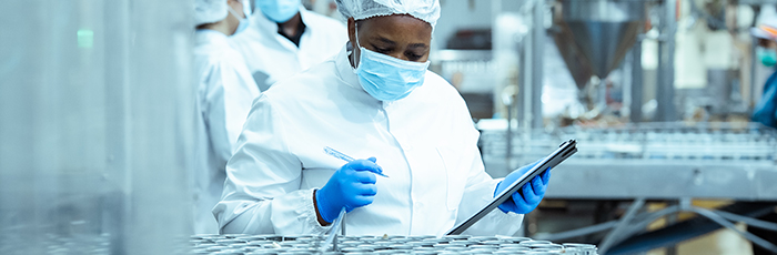 Factory worker performing factory audit with pen and clipboard in front of food cans
