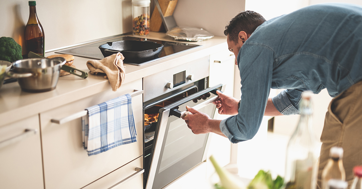 Man in kitchen opening oven door checking food