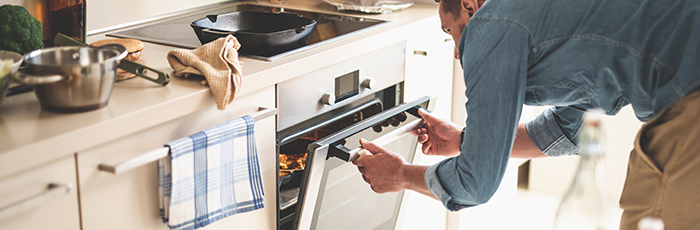 Man in kitchen opening oven door checking food