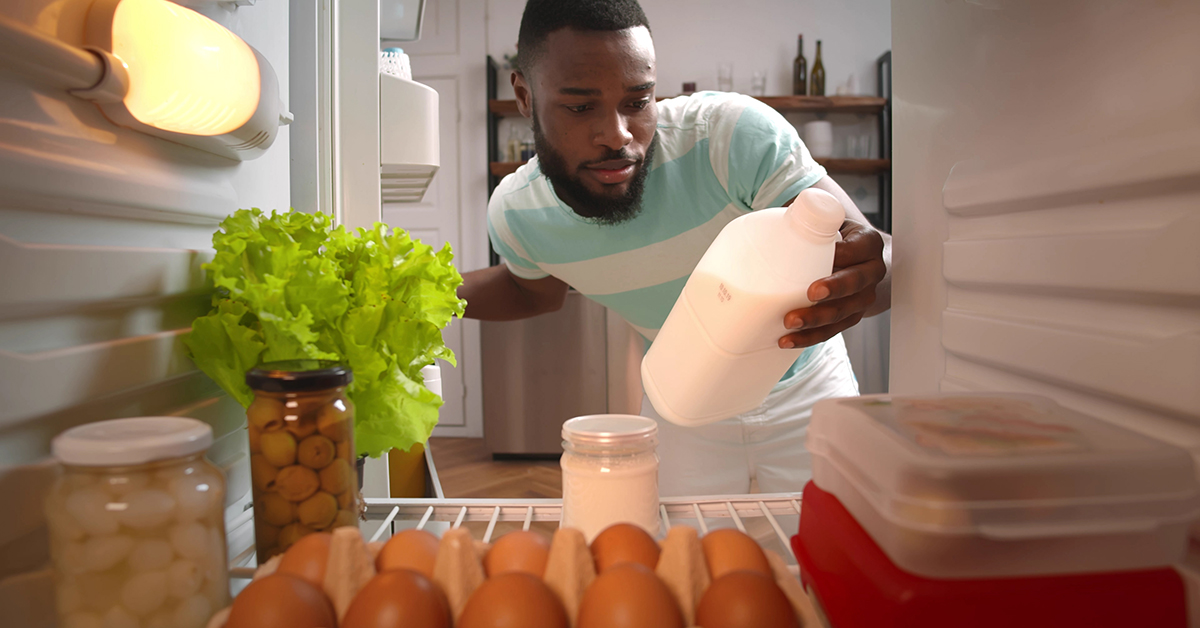 Man taking opened milk bottle out of home fridge