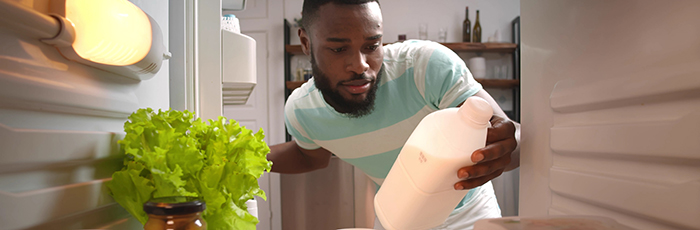 Man taking opened milk bottle out of home fridge