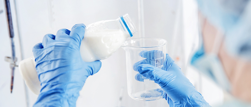 Scientist testing milk in laboratory. Scientist is pouring milk into glass jar