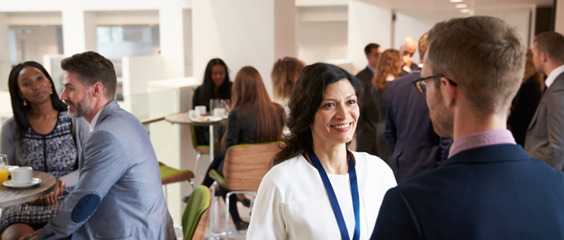 People networking at event. Man and woman talking in foreground.