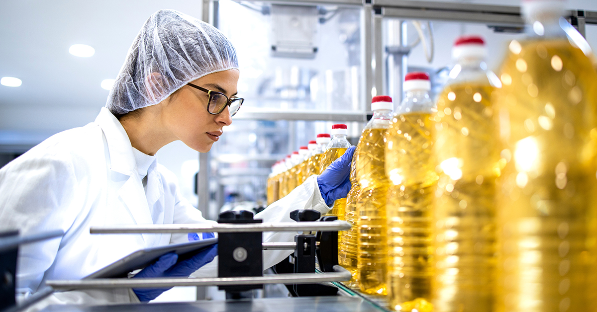 Cooking oil being inspected by woman in protective clothing and hair net with electronic tablet