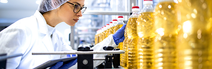 Cooking oil being inspected by woman in protective clothing and hair net with electronic tablet