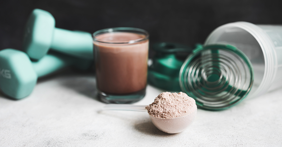 Protein powder with chocolate milkshake and exercise equipment in background
