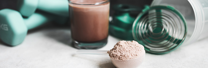 Protein powder with chocolate milkshake and exercise equipment in background