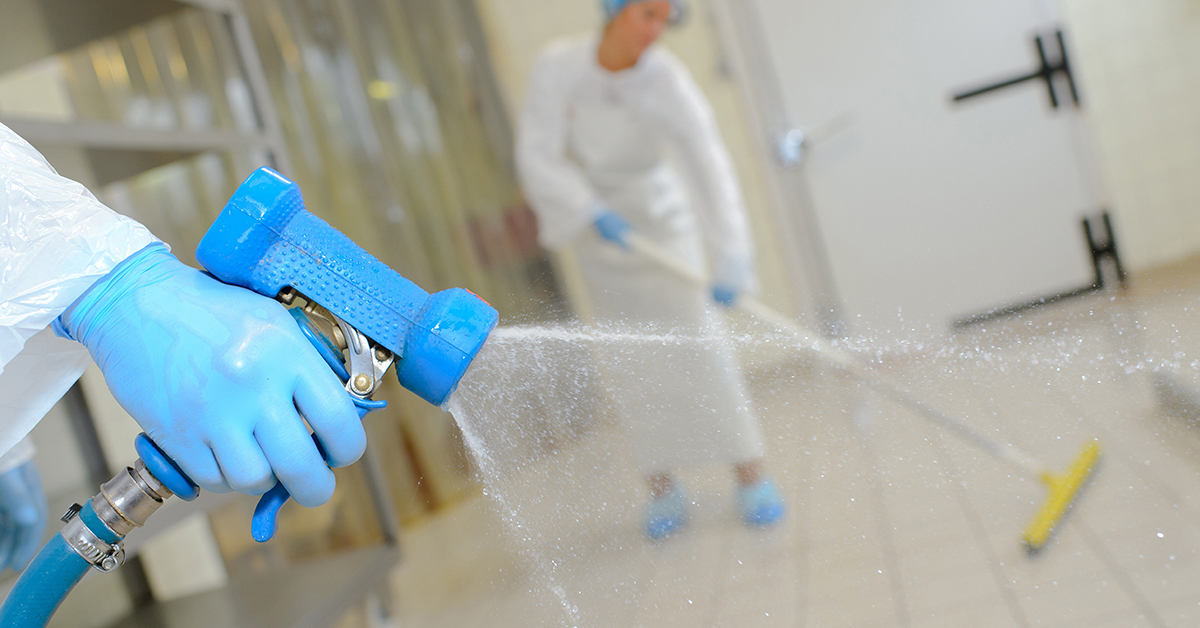 Factory working spraying factory floor with factory working scrubbing in background